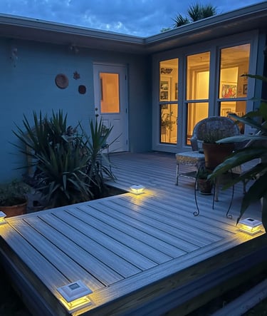 Illuminated modern composite deck with solar post cap lights in a backyard at dusk.