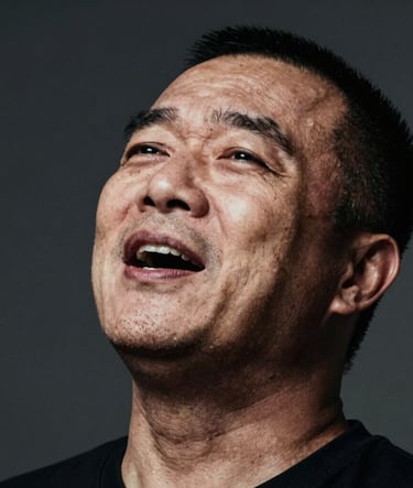 A high-contrast, artistic close-up of the tenor mid-performance, head tilted back slightly in a moment of vocal passion. Lighting is dramatic, highlighting facial features against a dark anthracite background. Subtle textures of sand and earth tones in the highlights.