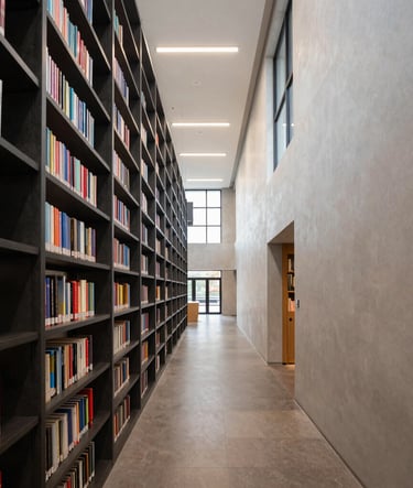 Wide-angle architectural photography of a modern library interior. The composition uses leading lines and natural light. Elements of Dark Slate shelving and Pale Frost walls create a sophisticated, academic atmosphere.