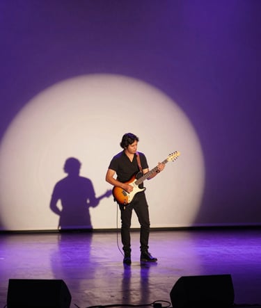 A wide-angle photography of a South American male musician on a minimalist stage holding an electric guitar, dramatic cinematic lighting with deep purple shadows and cream highlights, reflecting a contemporary pop and rock atmosphere.