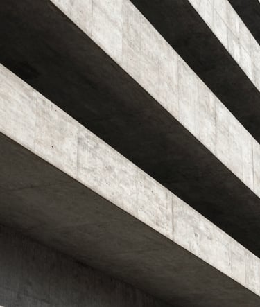 A close-up architectural shot of sharp concrete angles and deep shadows in a modern building in Rotterdam. The composition is minimalist, using charcoal and off-white tones to create a premium, geometric feel. Premium photography style.