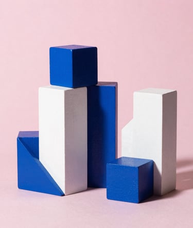 Still life photography of geometric wooden blocks painted in cerulean blue and white against a soft pink backdrop. Professional studio lighting with sharp, artistic shadows, reflecting Bauhaus precision in a North American / US setting.