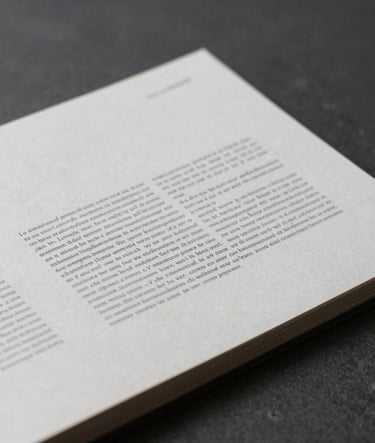 Desaturated, close-up photography of a printed editorial layout on high-quality paper, showing minimalist typography and clean lines, placed on a deep charcoal surface.