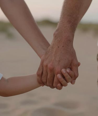 A close-up photograph of a family's hands joined together, showing a mix of adult and child hands. The scene is outdoors in North American / US (West Michigan) dunes at dusk. The palette includes Sand and Muted Rose colors with a soft, warm glow.