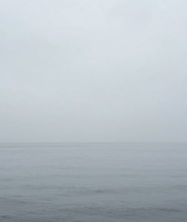 Contemporary photography showing a minimalist horizon where a calm gray sea meets a misty sky. The palette uses #D0D5DB and #F5F7FA to create a seamless, immersive atmosphere.