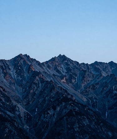 A panoramic alpine landscape at dusk, featuring sharp mountain peaks in steel blue and deep charcoal against a pale ice blue sky, clean minimalist composition, high-end fine art photography, International / Western.