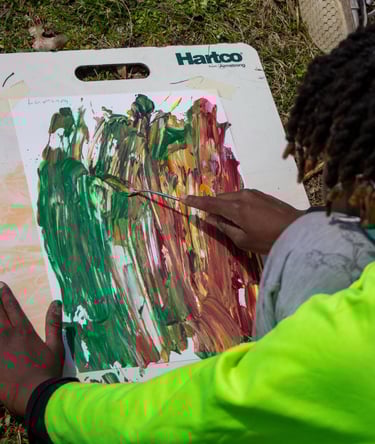 Young boy using a palette knife to smooth paint dabs over a paper.
