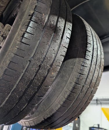 Close-up of worn car tires with uneven tread wear hanging on a vehicle lift in an auto repair shop.