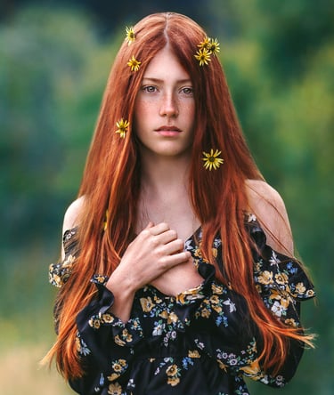 a girl with freckles and long red hair standing in a green field and has daisies on her hair