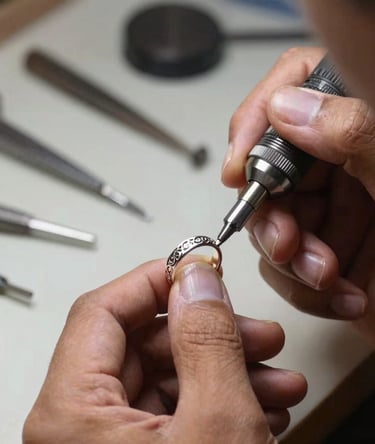 The hands of an Indonesian jewelry maker in a well-lit workshop, using a specialized micro-engraving handpiece to sculpt fine filigree details on a silver ring, with soft focus on steel tools in the background.