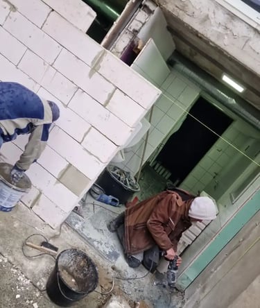Construction workers building a white aerated concrete block wall and using a power tool on a renovation site.