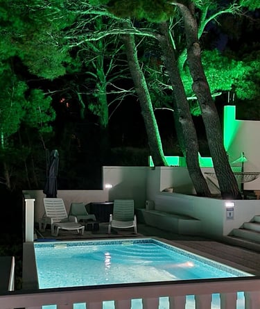 The photograph depicts an illuminated pool and part of the courtyard of Lokva Rogoznica's house.