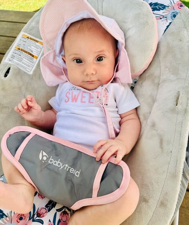 A newborn baby girl with a pink sunhat sitting in a bouncer, looking at the camera