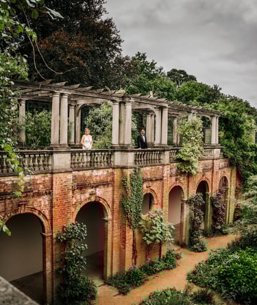Bride and groom standing on a terrace of a historic brick building surrounded by greenery