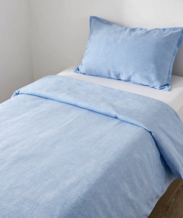 Light blue patterned duvet cover and pillowcase set on a white twin bed frame.