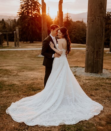 A bride in a lace wedding dress and groom embrace at sunset