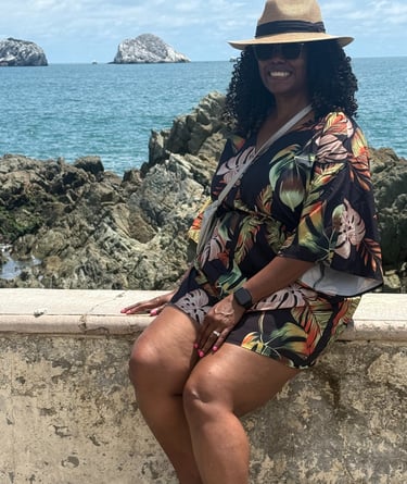 A woman in a hat and a hat sitting on a ledge with the ocean in the background