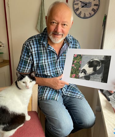 a man holding a pastel painting of his cat, with his cat sitting next to him