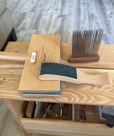 Fiber prep tools on a wood bench.  Includes carders and a comb