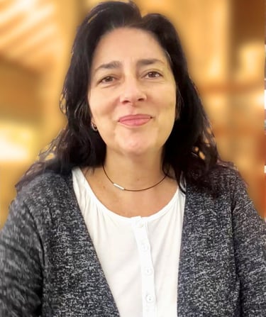 Smiling woman with long dark hair wearing a grey cardigan and white blouse in a professional setting.