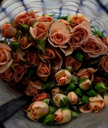 A fresh bouquet of peach spray roses and green buds wrapped in decorative blue mesh.