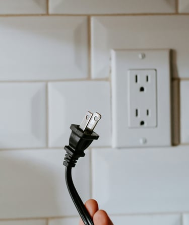 An electric cord being pulled out of the wall to prevent phantom energy.