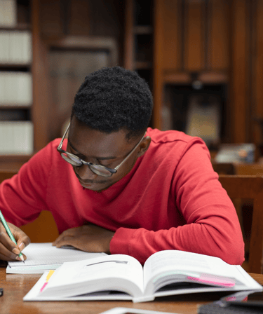 Un jeune homme écrivant dans un carnet tout en étudiant un livre ouvert, symbolisant réflexion