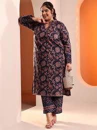Plus size woman in a dark floral print kurti set and matching trousers, holding a small woven handbag.