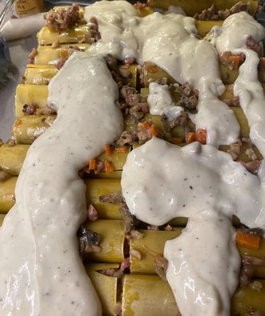 Uncooked cannelloni pasta tubes filled with meat and vegetable stuffing, topped with white bechamel sauce before baking.