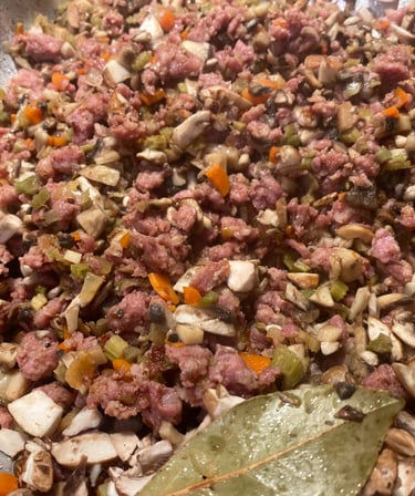 Close-up of savory ground meat, mushrooms, and vegetables cooking in a pan, featuring bay leaves for rich flavor.