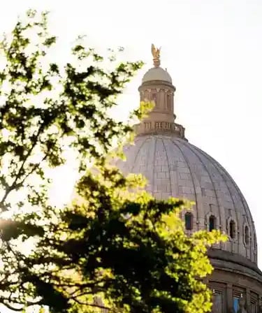 The Idaho State Capitol dome framed by green trees at sunset.