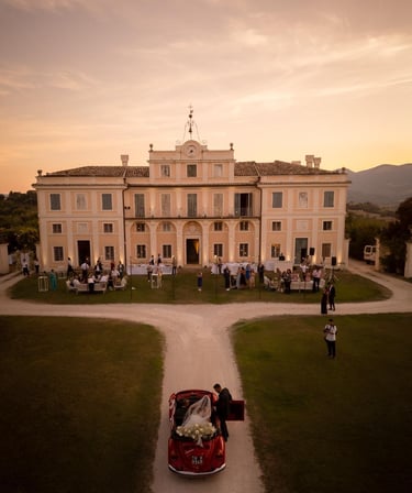 Arrivo degli sposi in auto d’epoca davanti a una villa storica illuminata al tramonto.