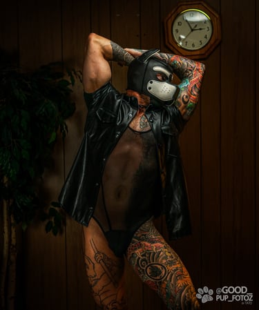 A tattooed man posing in a pup mask and leather vest.
