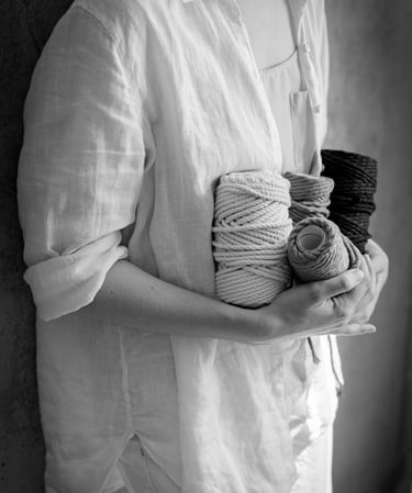 Black and white image of a person holding several spools of thick twisted rope, likely for macrame.