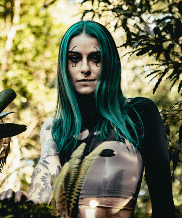Alternative woman with green hair and gothic makeup posing in a forest.