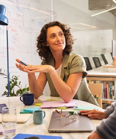 A smiling woman with curly hair participating in a collaborative office meeting at a round table.