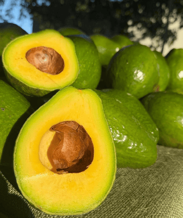 Fresh ripe green avocados halved to show yellow flesh and brown pits at a market.