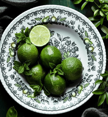 Fresh green limes and mint leaves on a vintage floral pattern ceramic plate with a lime slice.