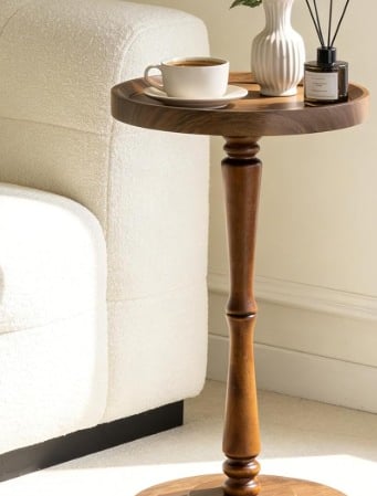 Round dark wood pedestal drink table or accent side table next to a white sofa.