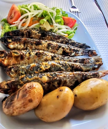 Five perfectly cooked Portuguese sardines served with salad and potatoes on a plate.