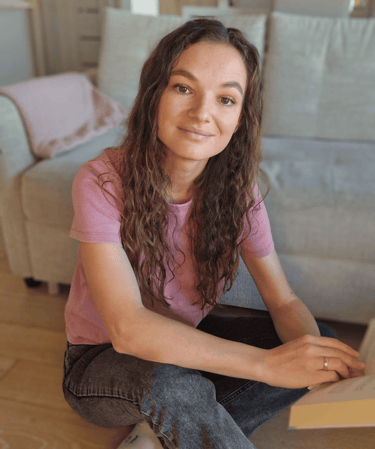 Psichologė Irma Chmieliauskienė. Tamsiaplaukė moteris sėdinti ant grindų su atversta knyga