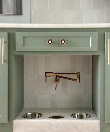 Built-in pet feeding station with stainless steel bowls, a small faucet and soft green cabinetry for
