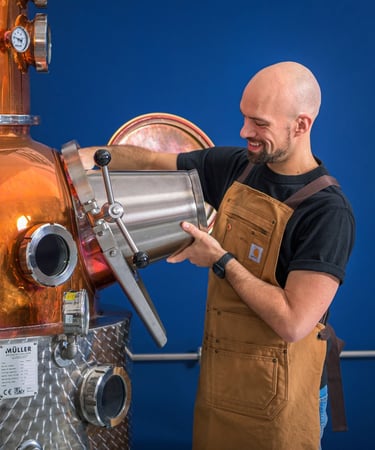 Mastro distillatore che sta caricando il suo alambicco con un secchio di acciaio in mano