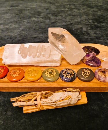 A variety of crystals placed on a wooden tray, with bundle of palo santo, sage and rosemary in front