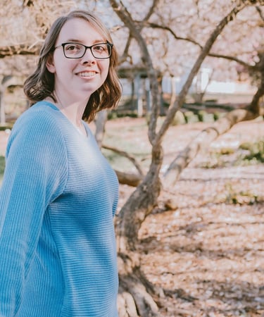Kristin Gunner, virtual assistant, in glasses and a blue sweater outside