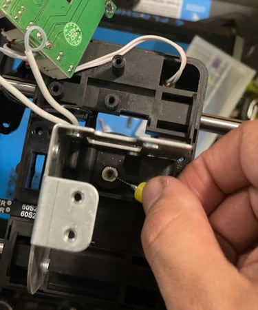 Hand clearing a clogged 3D printer nozzle using a fine needle cleaning tool.
