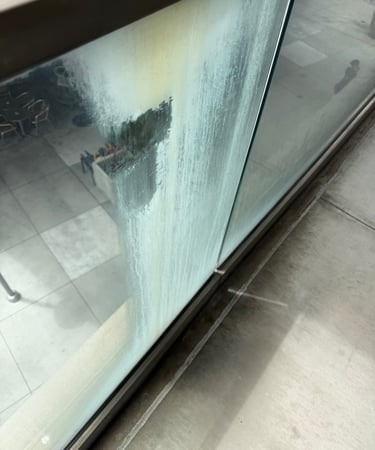 Cloudy condensation and mineral buildup on a commercial building glass window pane needing professional cleaning.