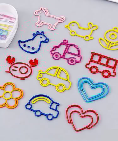 Collection of colorful novelty paper clips in shapes like animals, cars, hearts, and flowers on a grey surface.