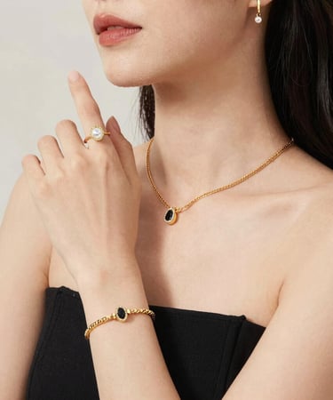 Elegant woman wearing a matching gold jewelry set with black onyx pendant necklace, bracelet, and pearl ring.