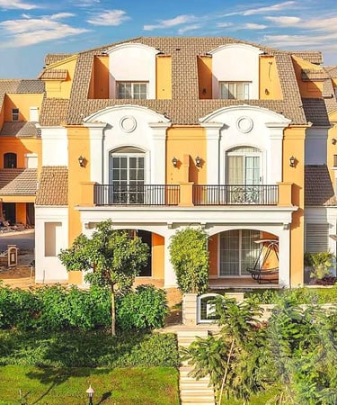 Luxurious yellow Mediterranean villa with white arches, balconies, and lush green landscaping.